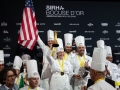 Team-USA-smiling-on-podium-holding-up-gold-statue-and-flag-TeamUSA_NOLA-542-photocredit_KenGoodman