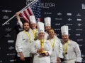 Team-USA-with-flag-and-statue-on-podium-TeamUSA_NOLA-567-photocredit_KenGoodman